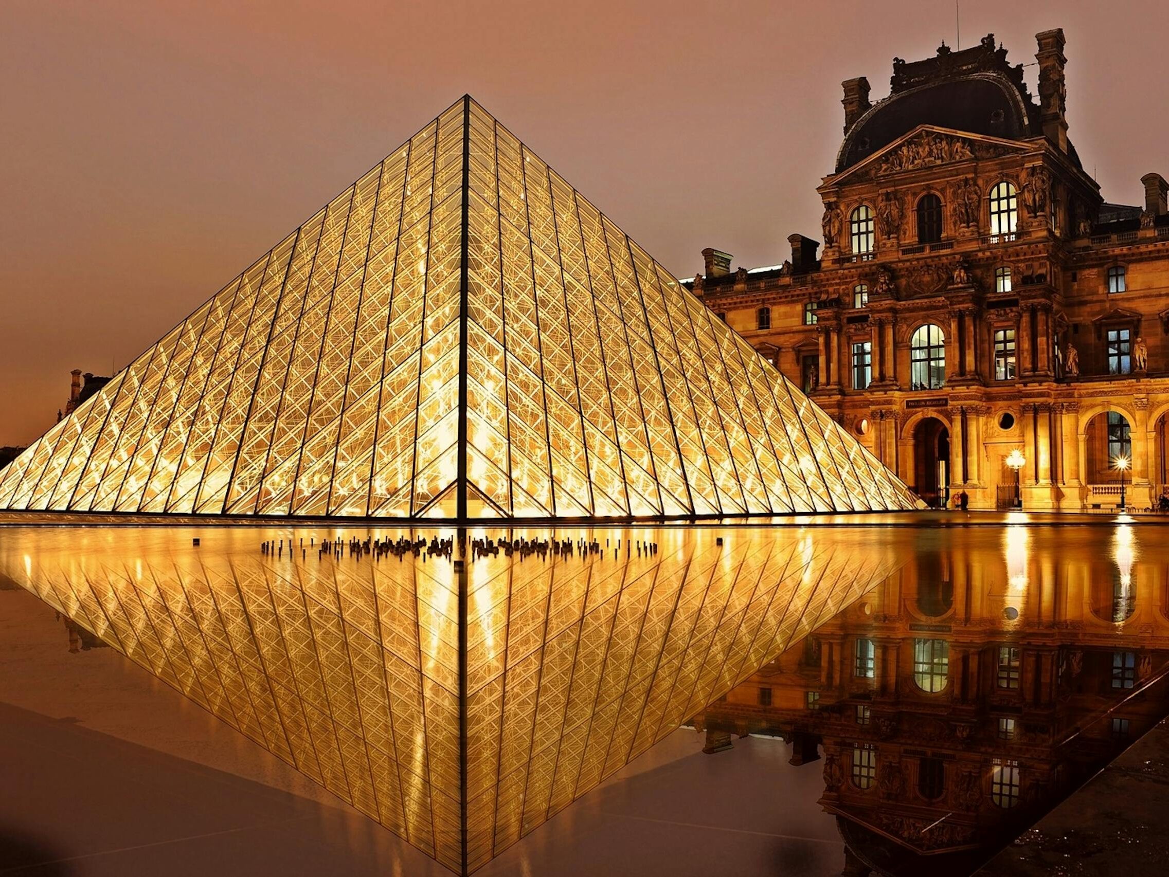 Stunning nighttime view of the illuminated Louvre Pyramid and reflection in Paris, France.
